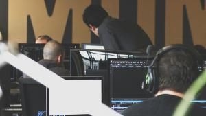 Photo of an office space with multiple workers using their monitors, with a supervisor looking over an employee's work